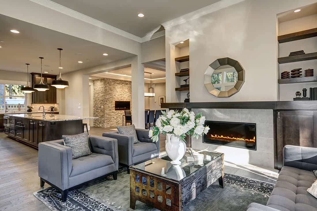 Chic living room filled with built-in cabinets flanking round mirror atop grey tile fireplace