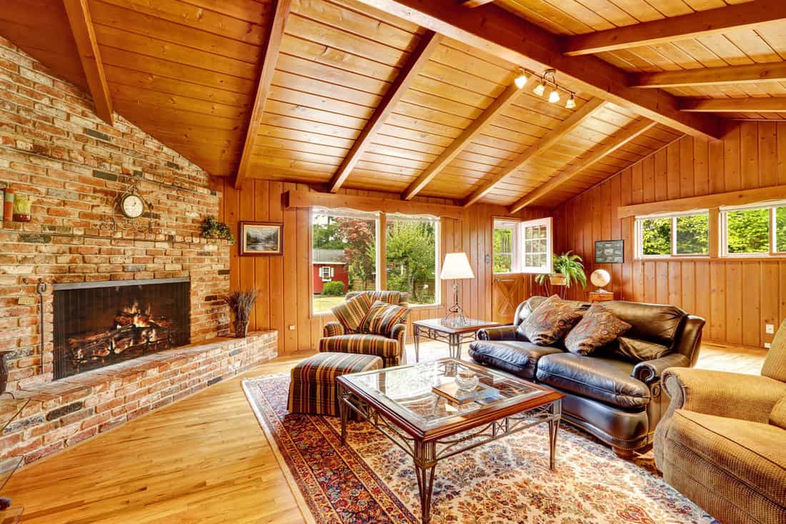 Log cabin house interior with vaulted ceiling. Luxury living room with fireplace, leather couch and glass top coffee table