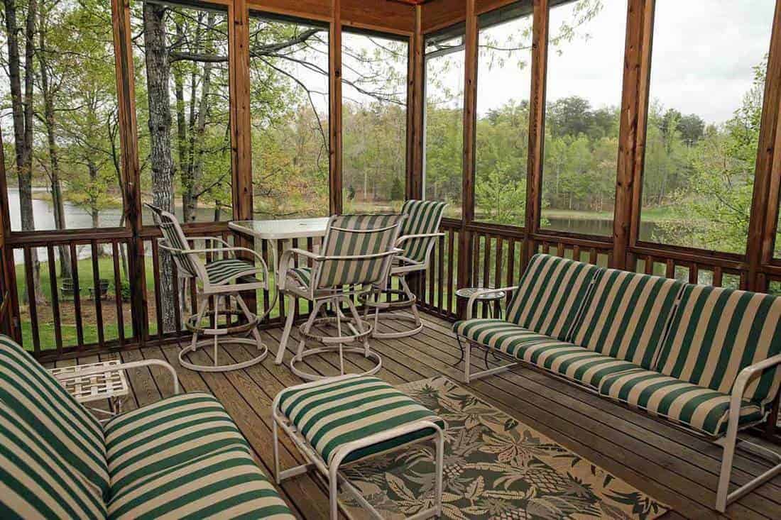 Screened porch on lakeside property with chairs striped with green, 18 Enclosed And Screened-In Porch Ideas [Photo Inspiration]