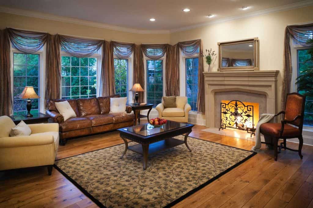 Lovely stylish well appointed living room with dark brown sofa, burning fireplace, elegant curtains and hardwood floors.