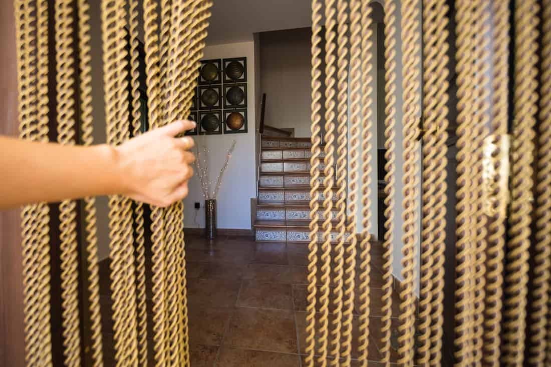 Woman shoving gold beaded curtain at doorway, 10 Fantastic Indoor Beaded Curtains For Doorways