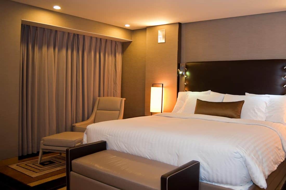 Une belle chambre avec une parure de lit blanche, un mur marron et un rideau de couleur beige clair