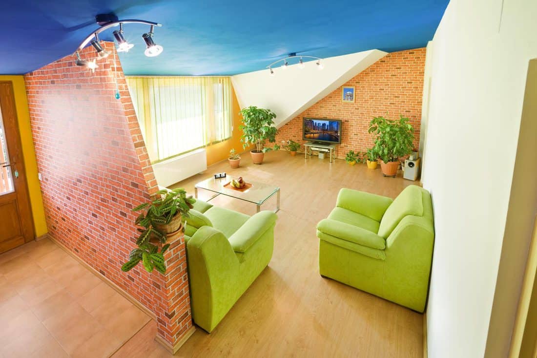 A modern living room with wooden flooring, green sofas, blue ceiling, and a brick patterned partition