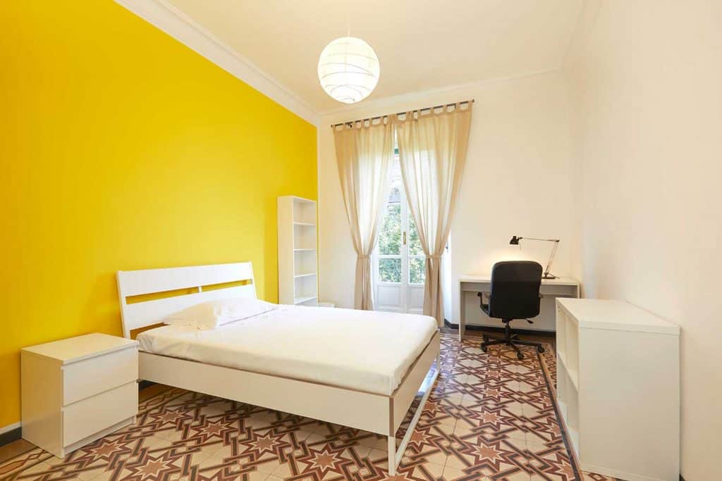 Chambre avec grand lit, bureau, murs jaunes et beiges avec rideaux beiges