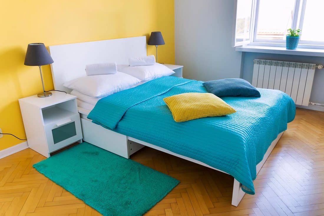 Bedroom with light blue and yellow colored walls and a bed with white pillows and a blue blanket