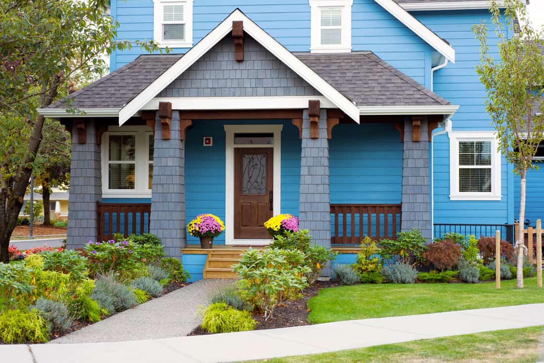 Blue walled front porch with brown door and garden on the side of the pathwalk