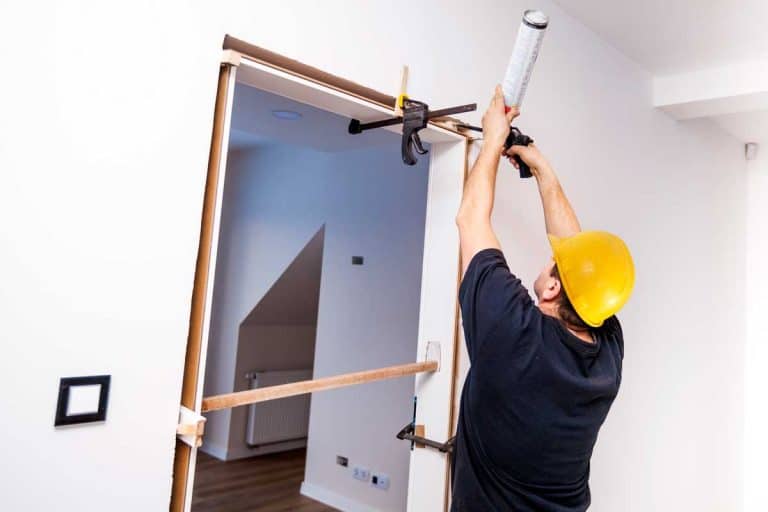 Construction worker installing door in home. Handyman installing door with an mounting foam in a room. Worker assembles the door frame. Does A Door Need A Frame?