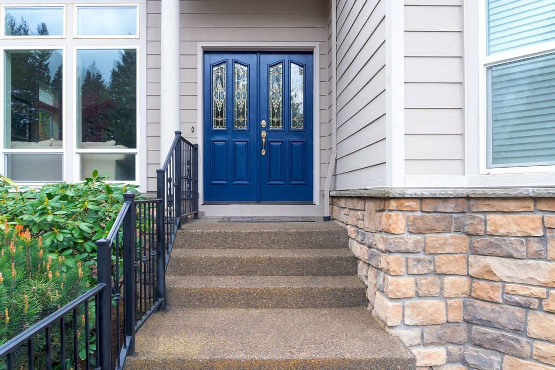 House front entrance with concrete steps iron rod railing and navy blue double doors