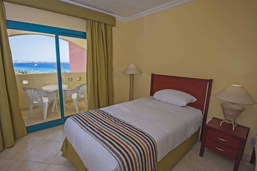 Design d'intérieur d'une chambre d'hôtel tropical de luxe avec murs et rideaux jaune moutarde, balcon et vue sur la mer