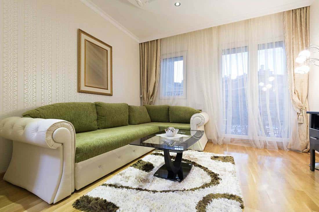 Interior of a luxury apartment living room with beige and green sofa set, beige curtains and painting 