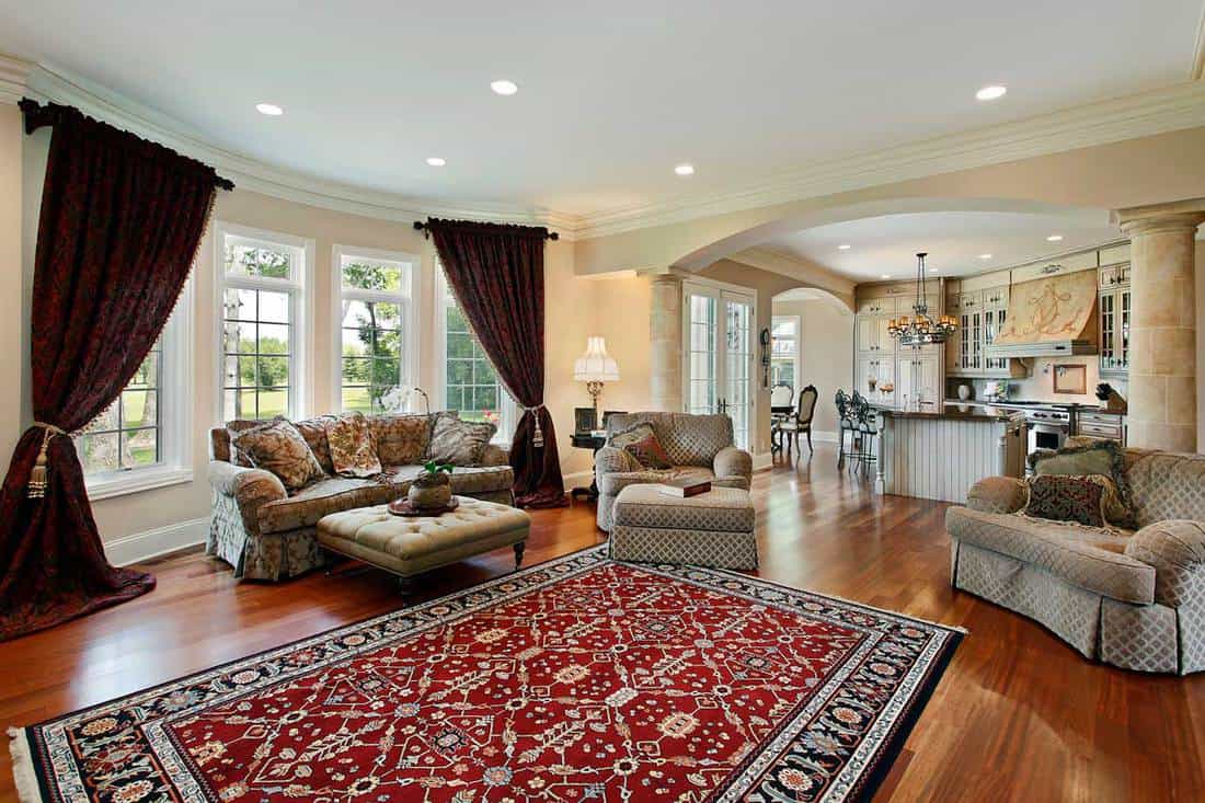 Living room with two columns, couches, chairs, and a border patterned (red, white and black) area rug at the center of parquet floor