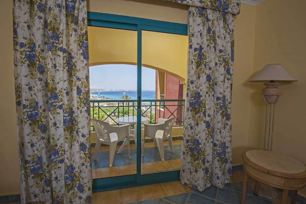 Chambre de luxe dans un hôtel tropical avec murs jaunes, rideaux floraux à proximité, balcon et vue sur la mer