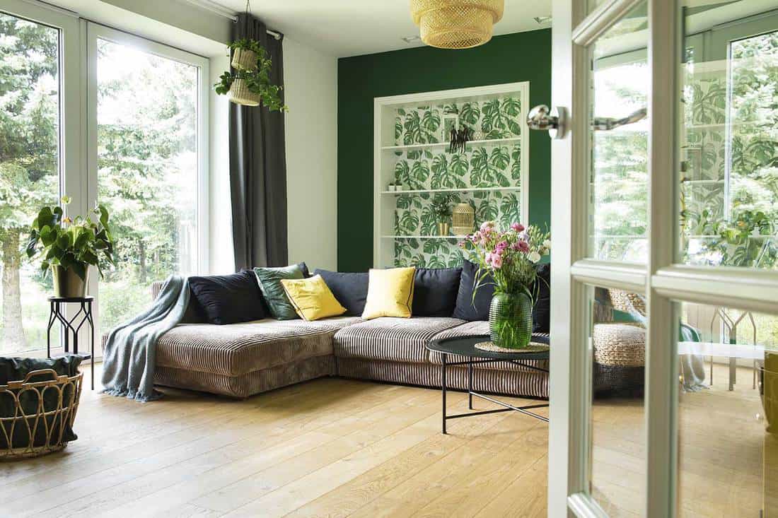 Salon moderne et confortable avec canapé en velours côtelé, oreillers, grande fenêtre sur le jardin