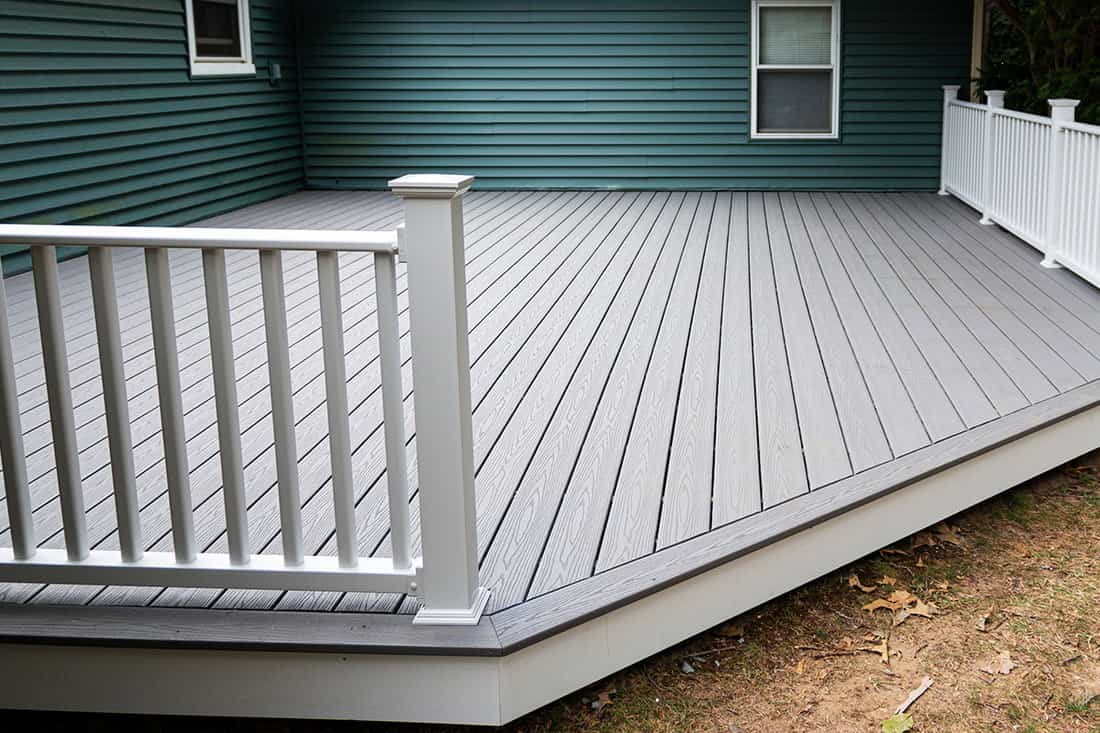 New composite deck on the back of a house with green vinyl siding and flooring