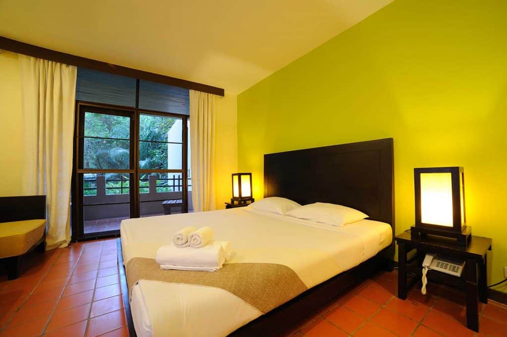 Chambre d'hôtel tropicale avec balcon, murs jaunes, rideaux jaunes et carrelage rouge