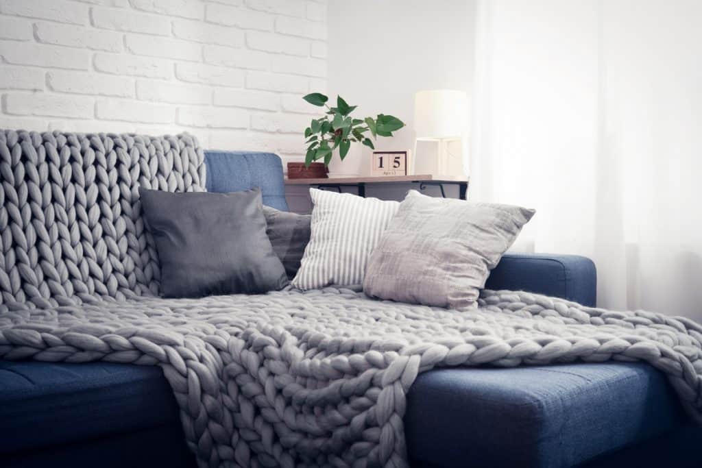 A blue colored sofa with a comfortable blanket and throw pillow placed on top