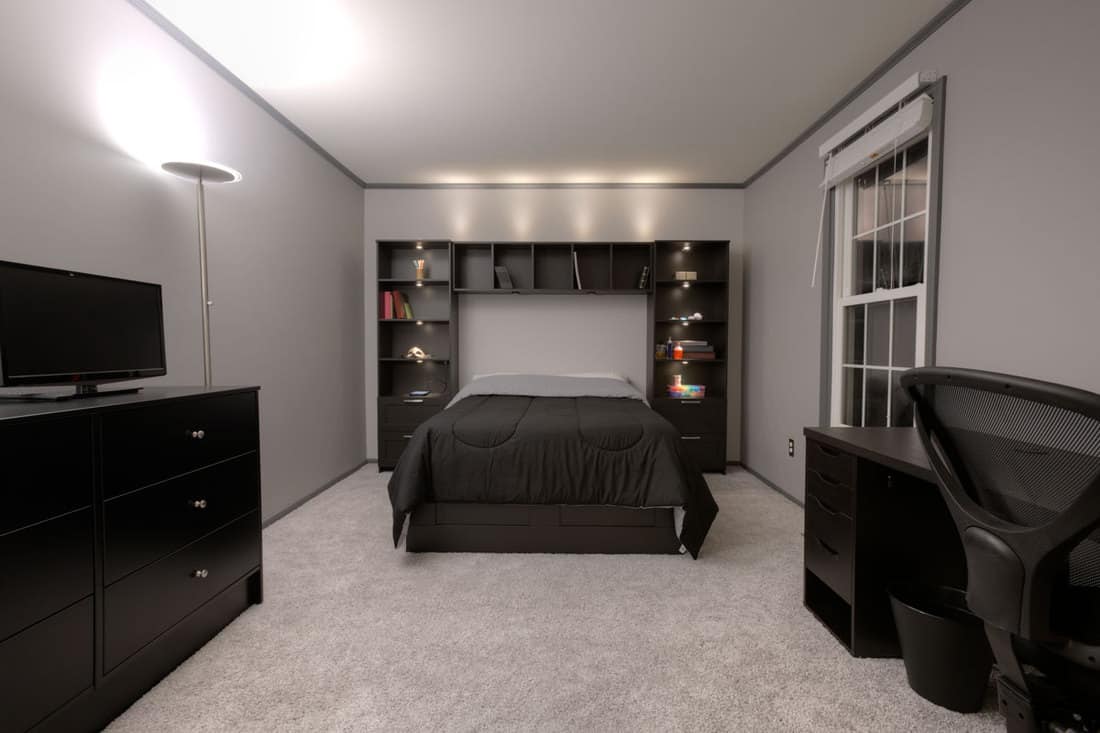 A gray colored living room with a black furnitures and appliances and a black bed with a black bedding sets