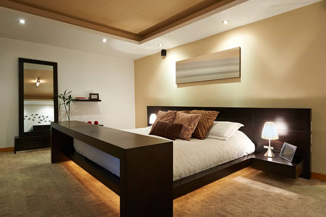 A modern bedroom with a table in front of the bed and a mirror on the side, How To Brighten Up And Decorate A Room That Has No Windows