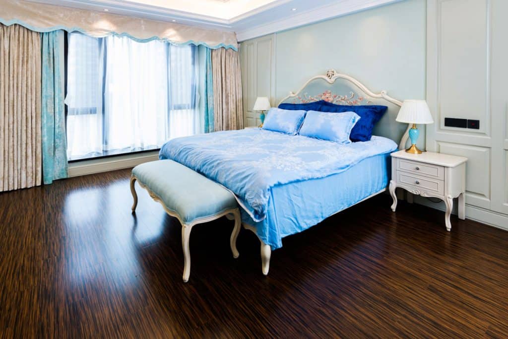 A white colored bedroom with a blue colored blanket and a blue colored curtain