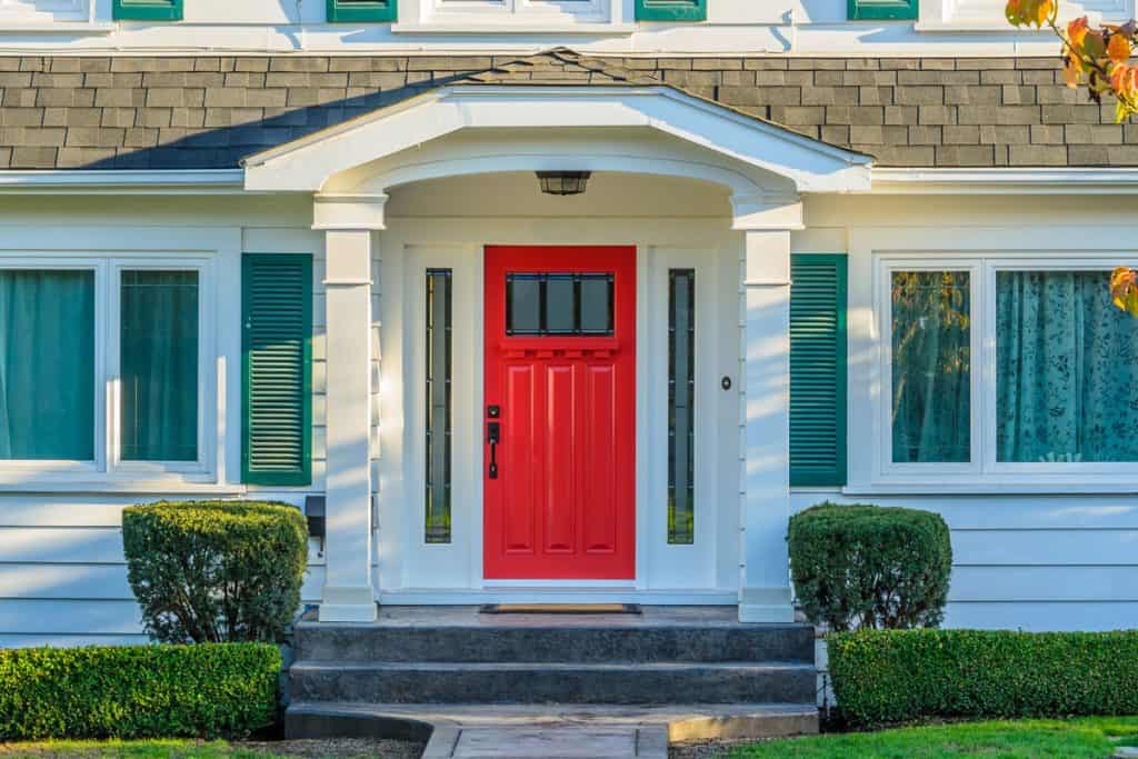 Bright red colored fron door with a matching white trim and torqouise window shutters