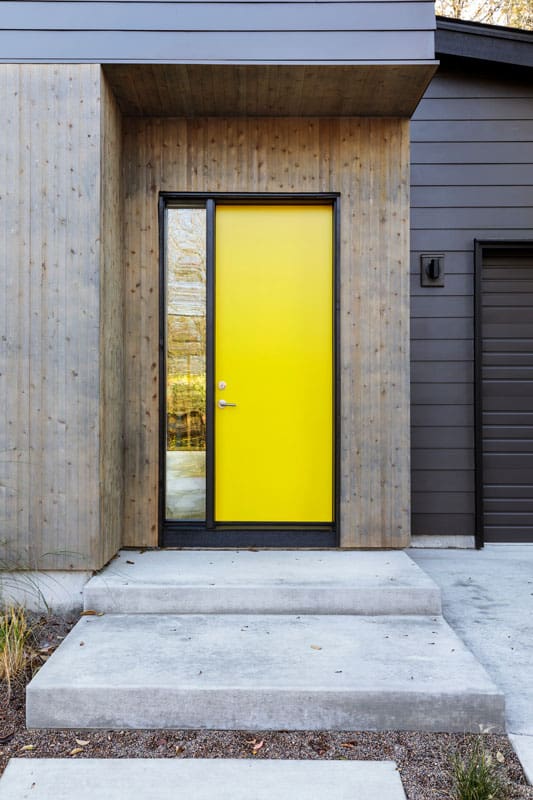 Bright yellow front door of a modern house with a small window pane on the side