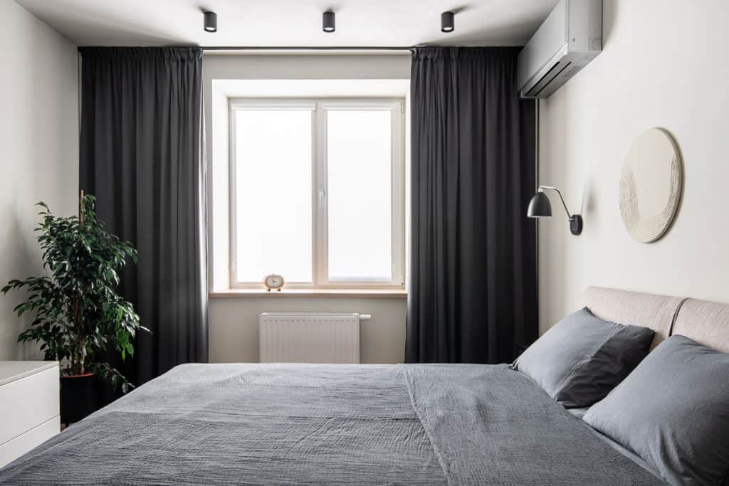 Dark black curtains inside a narrow modern bedroom with white painted walls