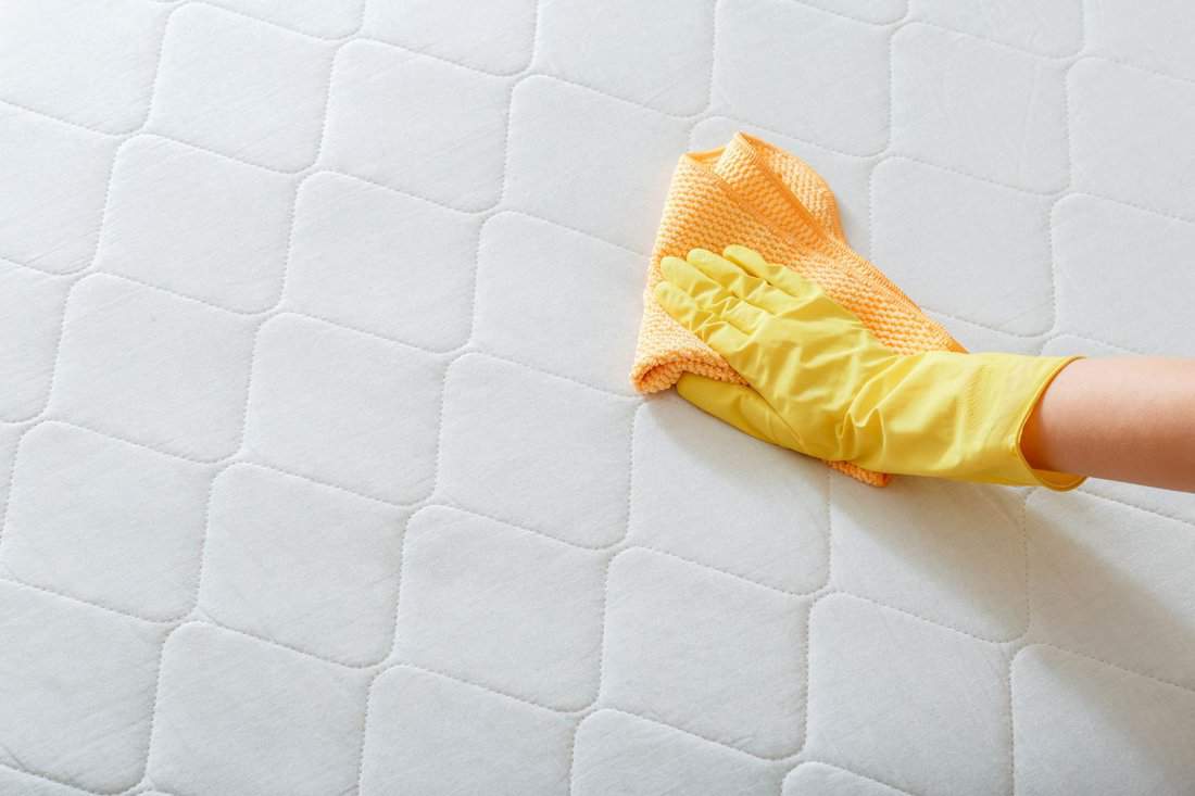 Employee cleans surface of mattress on bed with rag. Cleaning disinfection surfaces. Cleaning company person Hand in glove do Mattress chemical cleaning.