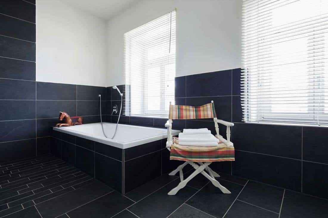 Interior of a modern black-tiled bathroom with white blinds