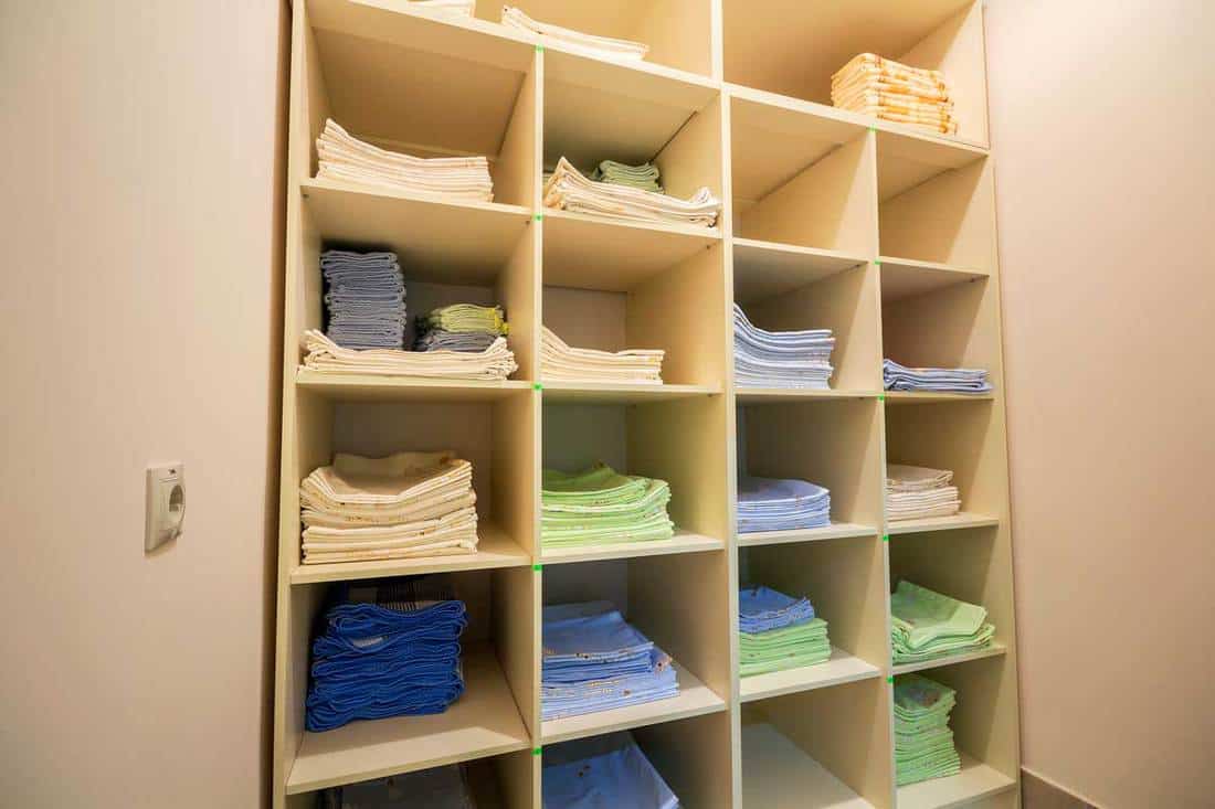 Interior of white plastic cabinet with stacked piles of clean colorful linen on shelves, How to store linens 4 easy solutions