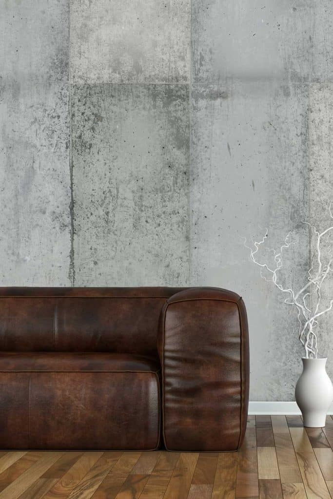 Living room with brown leather sofa on hardwood floor and grey concrete wall background