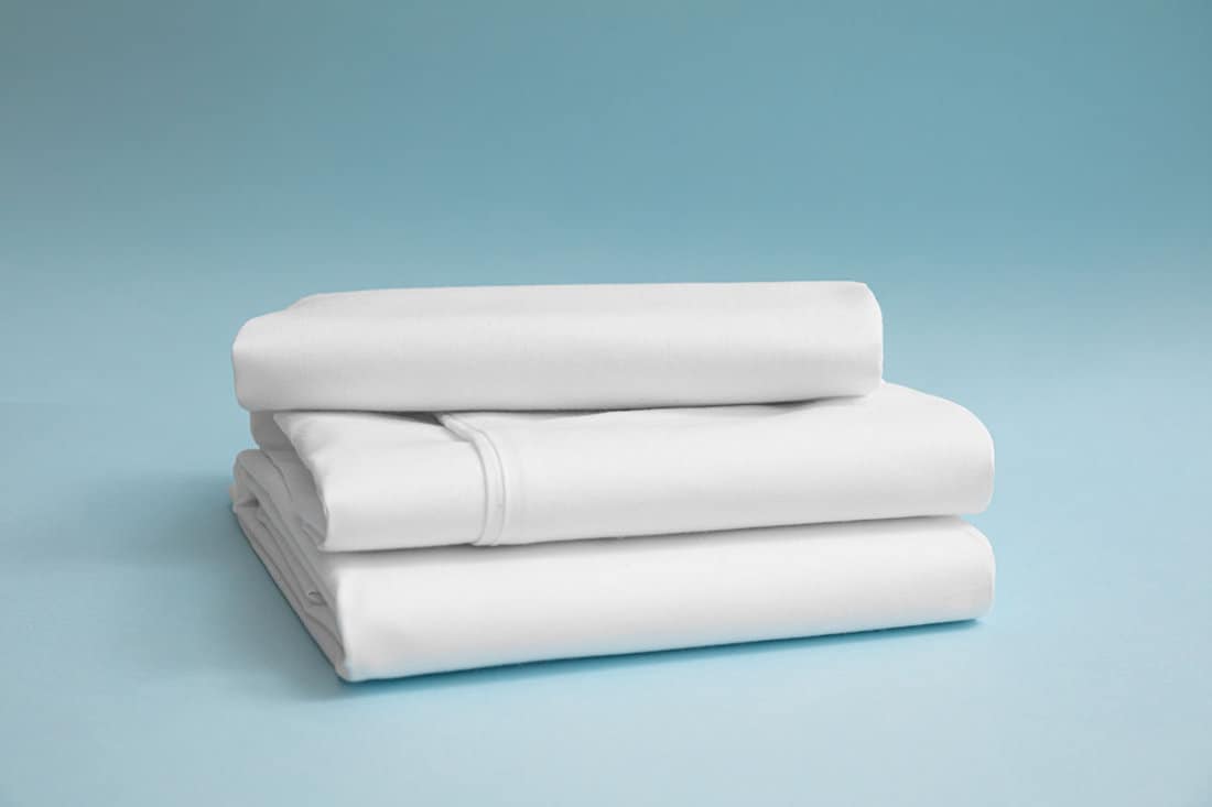Stack of white bedding against blue backdrop, folded soft bed clothes, stack of white cotton sheets