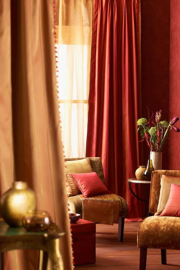 Vintage themed living room with comfortable chairs, pink and brown throw pillows, and a red floor length curtain