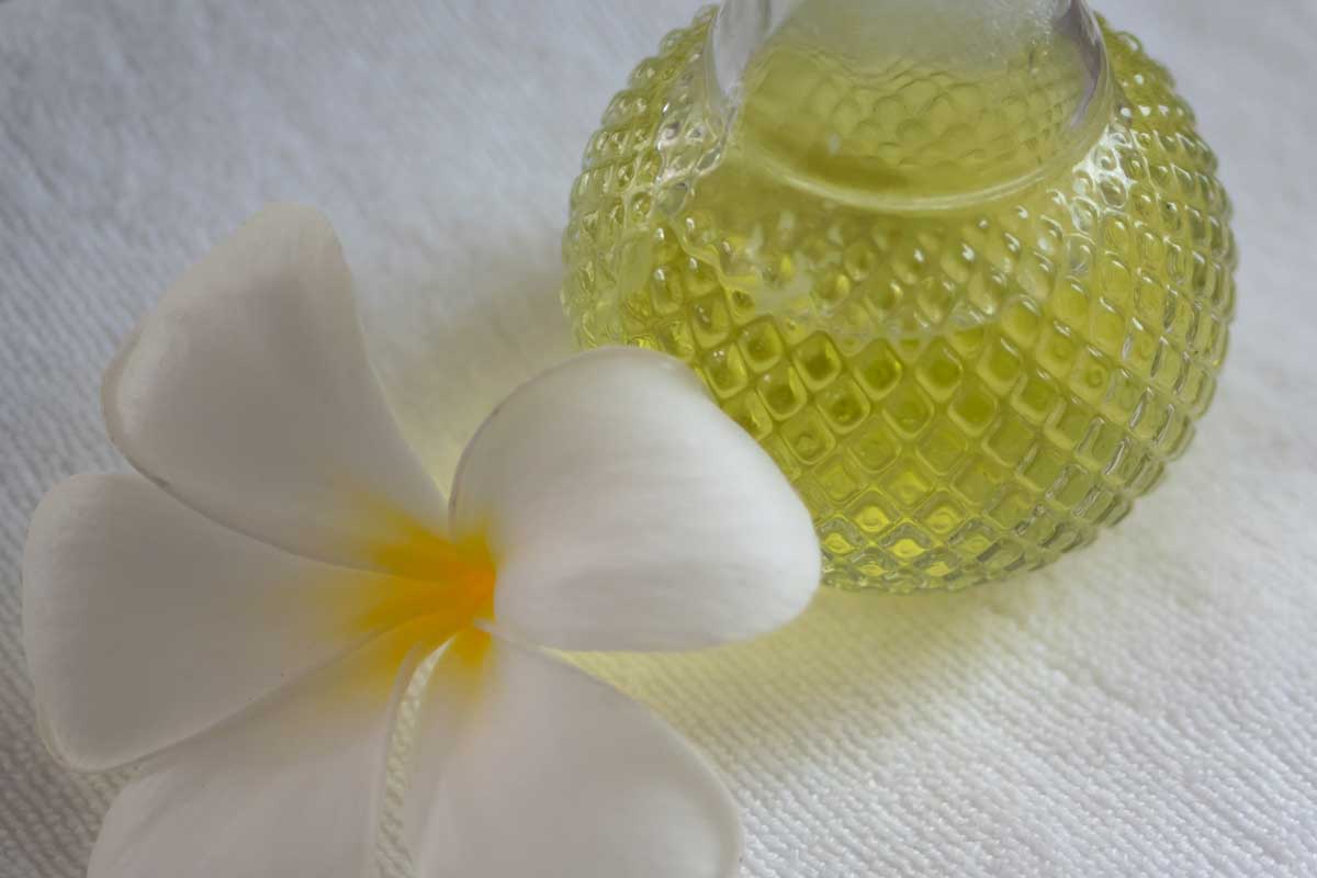White plumeria flower and oil bottle on bed with white sheets