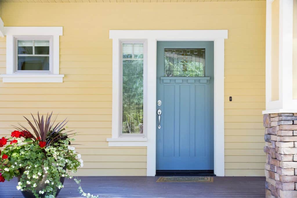Yellow house siding with white trims and a blue front door