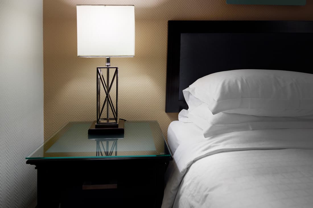 A modern designed lamp placed on a nightstand beside a bed, Do You Need Two Nightstands? [Design rules and suggestions]