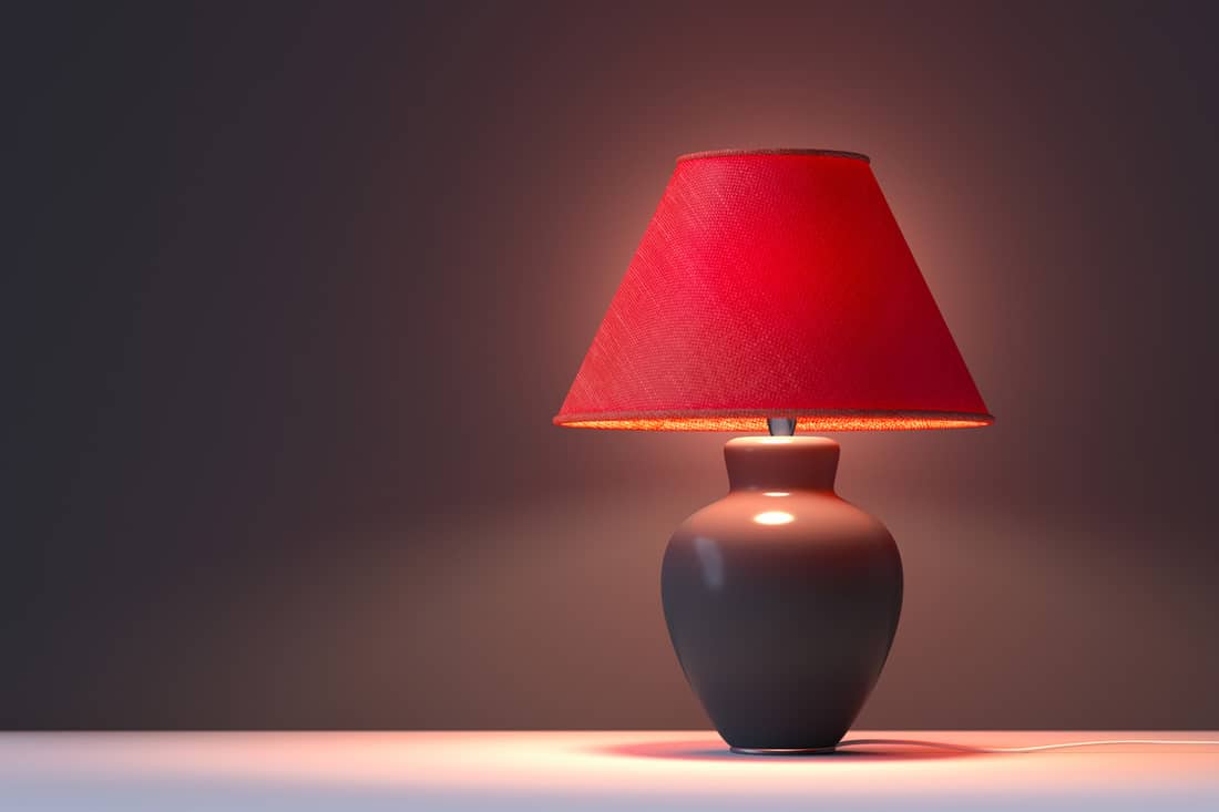 A red colored lamp shade turned on with a gray background, Can You Wash Lamp Shades in the Dishwasher?