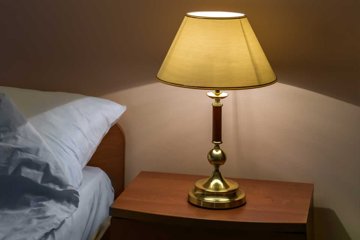 Classic lamp with turned on bulb under lampshade against wall in bedroom, Why Does My Lampshade Look Yellow? [And how to reverse the effect]