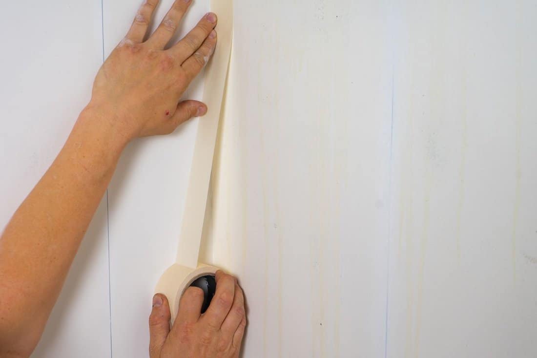 Human hands holding adhesive tape and preparing for painting.