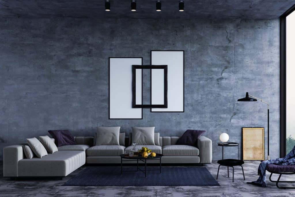 Interior of a dark bluish gray themed living room with spot lights and a gray sectional sofa matched with a blue carpet