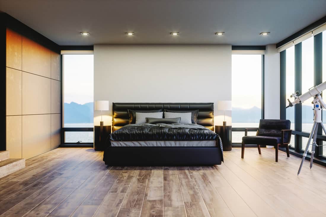 Modern bedroom with a panoramic view of the ocean visible with its huge windows paired with a luxurious dark themed bed and a concrete covered headboard, Do Beds Need a Headboard? [The answer may surprise you!]