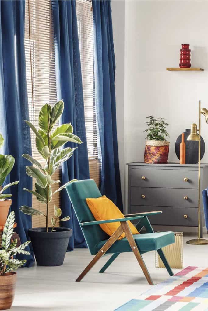 Oreiller orange sur un fauteuil vert près d'un canapé bleu dans un intérieur de salon coloré.