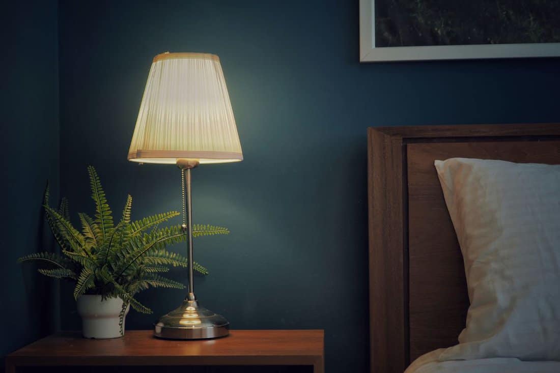 Vintage​ side bed​ lamp​ on​ the​ wooden​ bedside table.​ Retro bed​ room interior​ design.