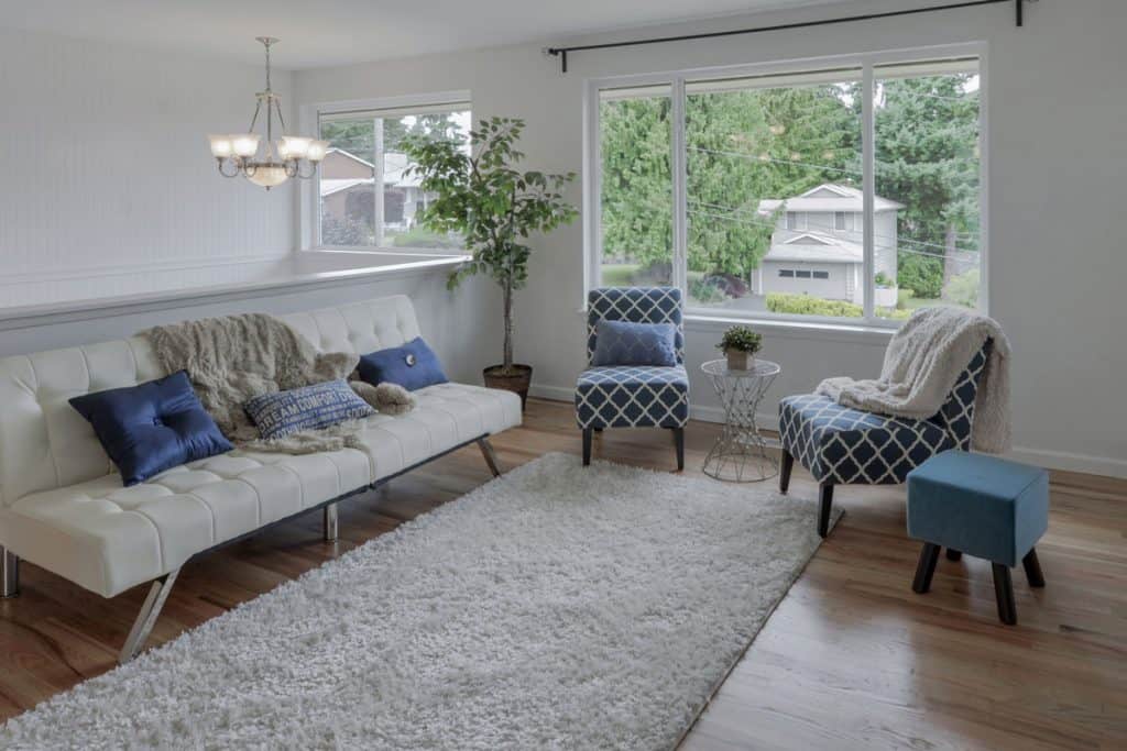 White sofa with blue throw pillows inside a minimalist living room with white area rug