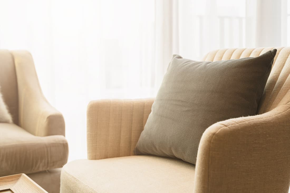 A beige fabric sofa with a gray throw pillow