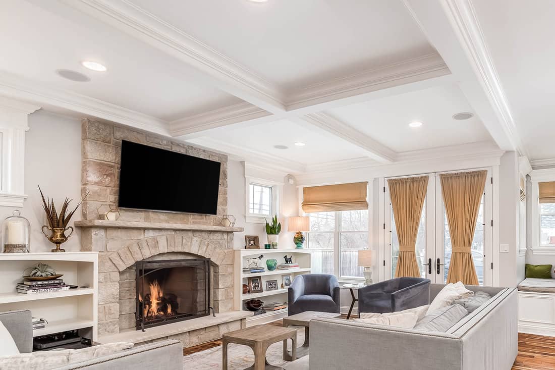 A cozy living room with a television mounted above a fireplace in front of couches and chairs