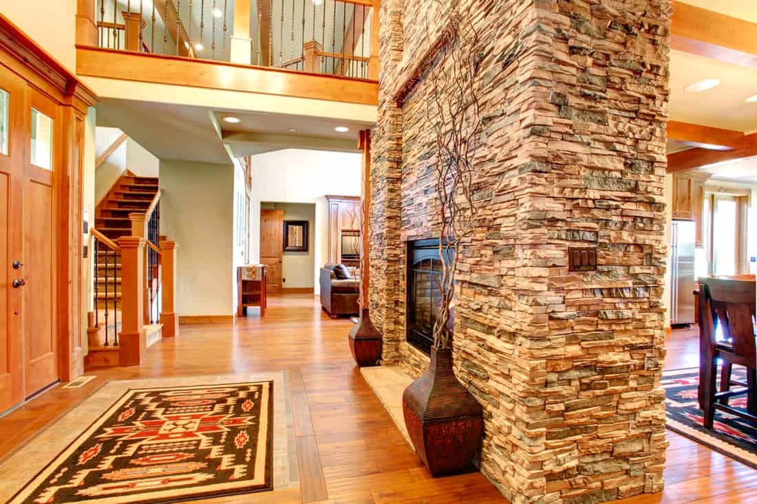 A decorative stone cover in the fireplace section with wooden flooring, Is Stone Veneer Worth It? Stone Interior Walls Pros and Cons