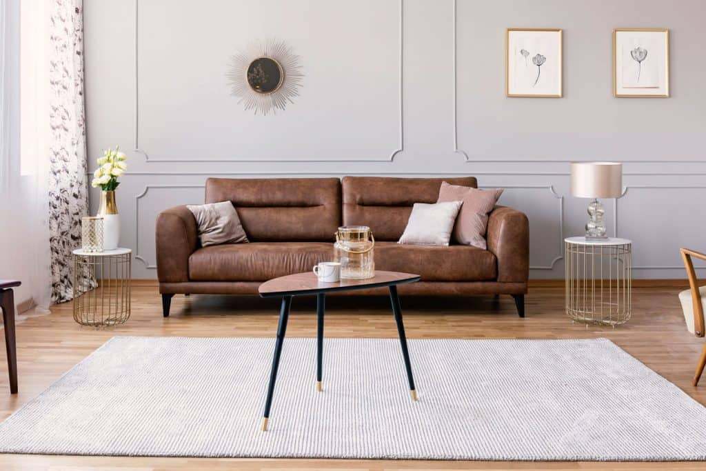 A leather sofa with white and brown throw pillows, a light gray carpet, and two end tables on each side
