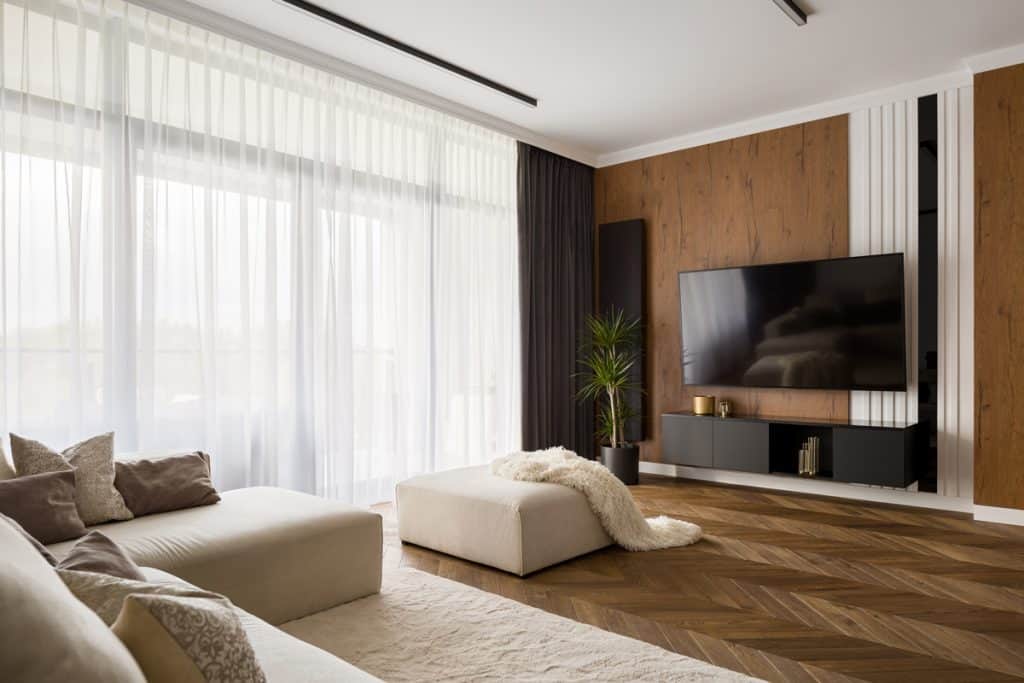 A luxurious modern living room with a brown wooden paneled wall on the TV section and a wooden paneled riser