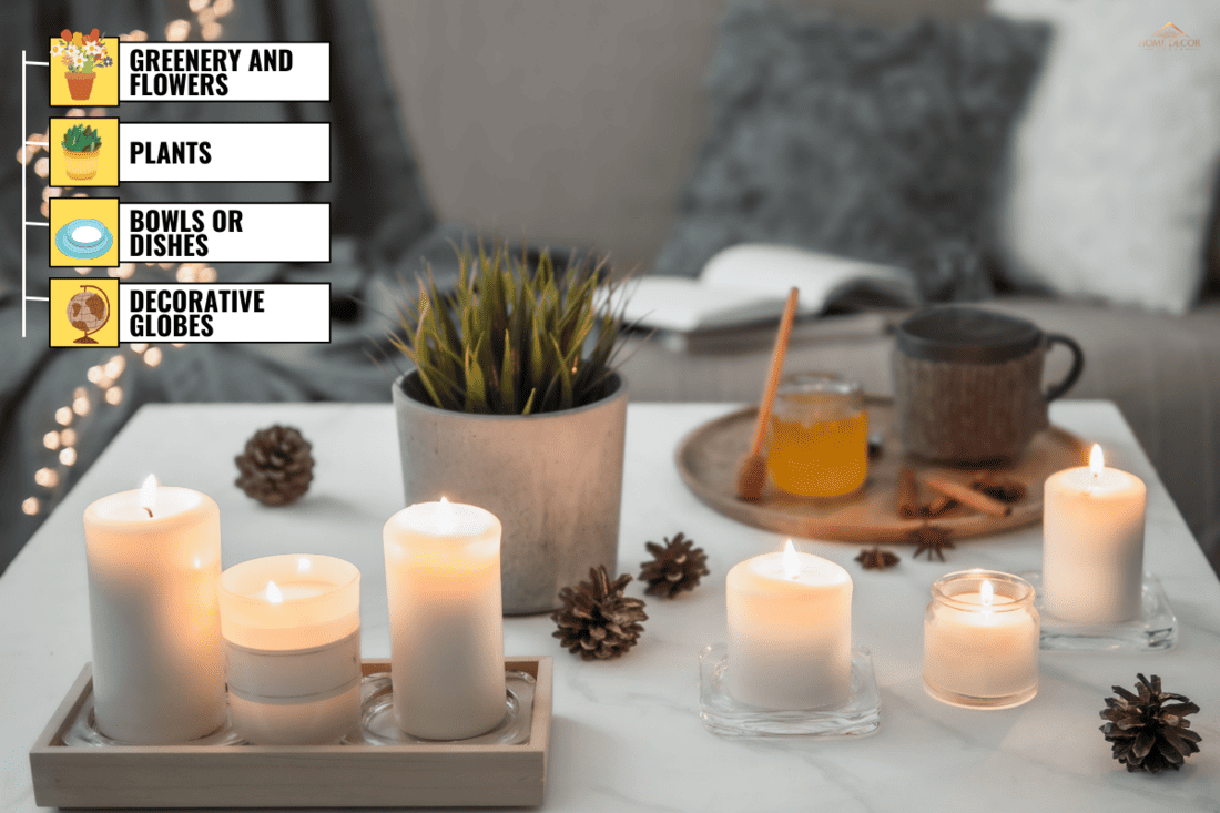 Cozy home, hygge, cosiness concept - burning white fragrance candles on white marble table near sofa with pillows and plaid. Winter decor, hot tea cup and honey. - What Can You Put In A Candle Holder Besides Candles?