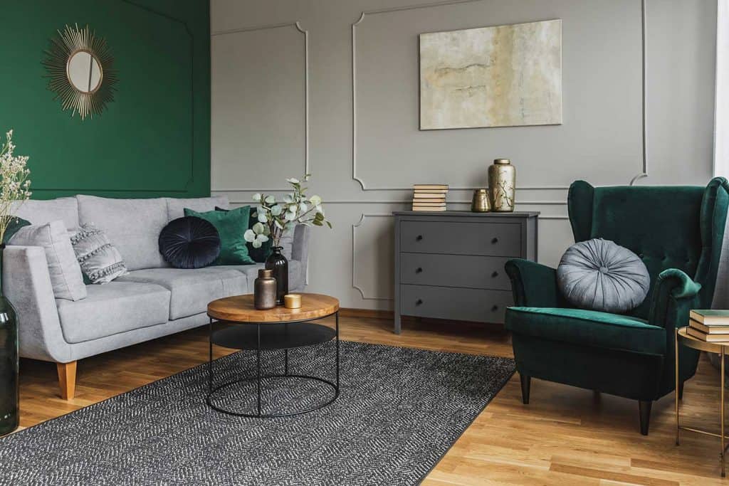 Chaise à dossier à oreilles vert émeraude avec oreiller à l'intérieur du salon gris avec commode en bois et tapis gris